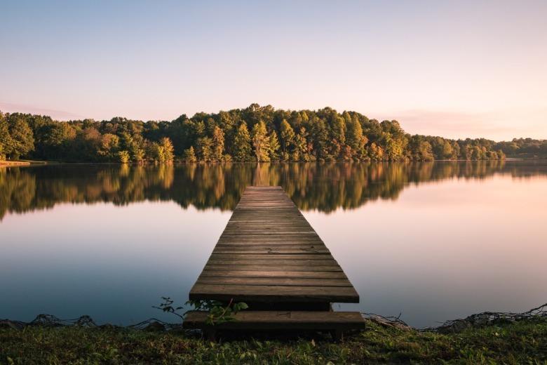 A wooden dock sits empty over a large body of water. The sunset casts an orange and purple glow on the water.