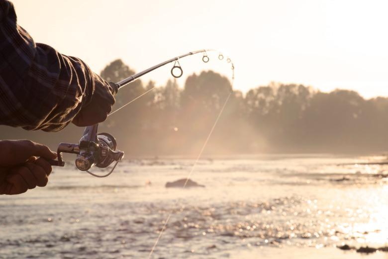 A close-up view shows a person holding a fishing pole that has been cast into a body of water. The fishing line is taut.