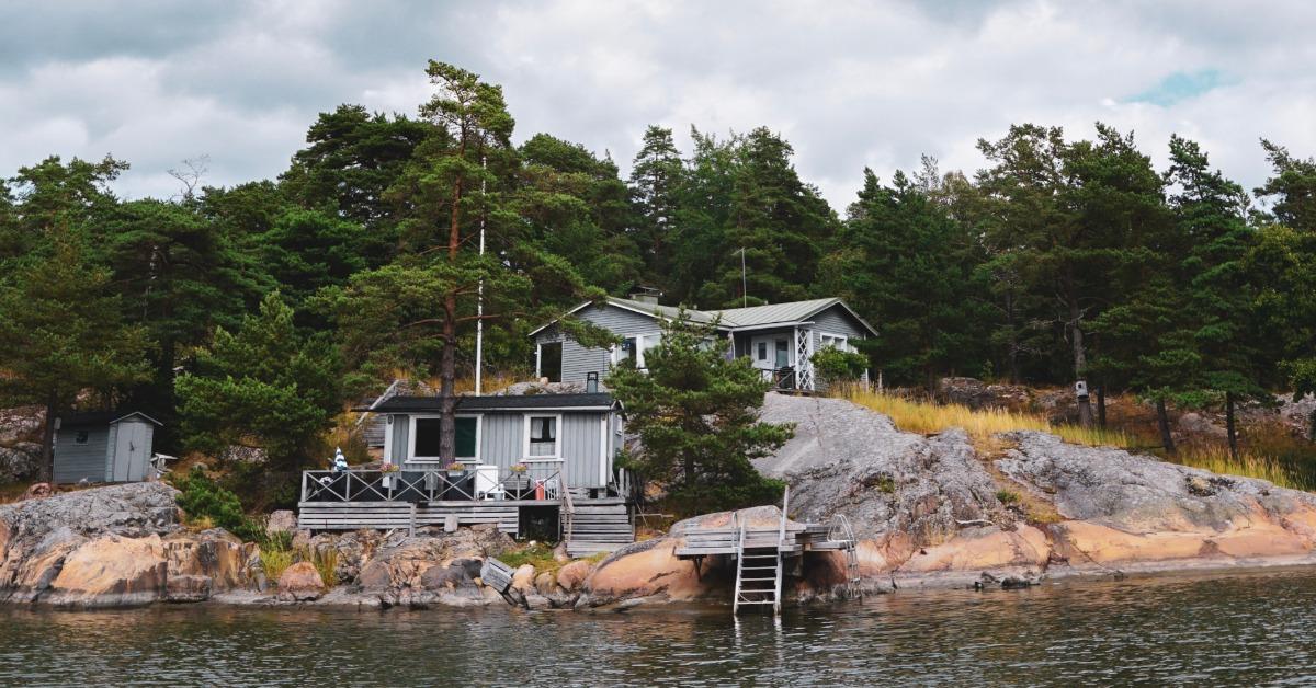 A group of small cabins sitting on a rocky shoreline above calm water, surrounded by a bunch of large trees.